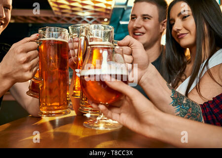 Messa a fuoco selettiva di pinte di birra nelle mani di felice giovani amici nel pub. Allegra compagnia insieme a riposo durante il fine settimana e di bere birra nel bar. Concetto di felicità e di bevanda. Foto Stock