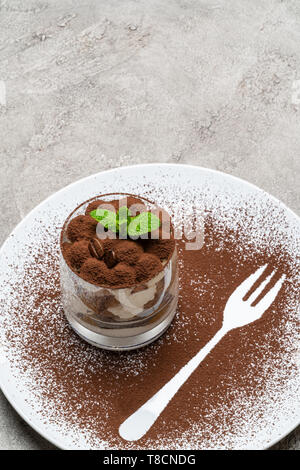 Tiramisù classico dessert in un bicchiere sulla piastra con sagoma a forcella su sfondo di calcestruzzo Foto Stock