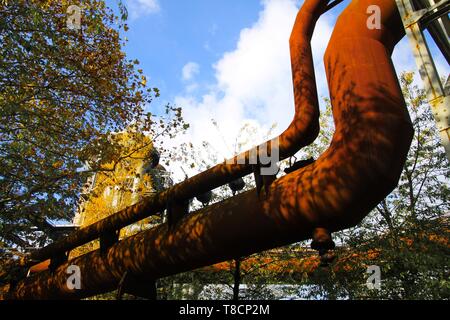 Landschaftspark Duisburg, Germania: basso angolo vista sulla curva isolata pipeline corrosi contro il cielo blu e alberi Foto Stock