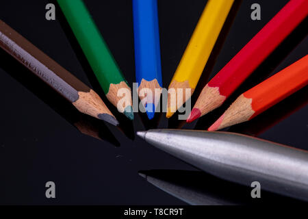 Le punte colorate matite in legno su uno sfondo nero con immagine speculare rispetto a una penna a sfera Foto Stock