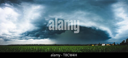 Vista panoramica di una terribile tempesta scuro avvicinando piccolo villaggio. Che scorre sopra i campi di mais. Foto Stock