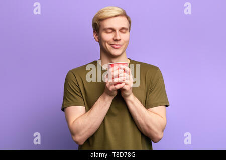 Awesome ragazzo con gli occhi chiusi gode di bere il tè, studio shot,Tempo libero Tempo libero, la felicità, l'uomo riceve piacere dal bere il caffè caldo Foto Stock