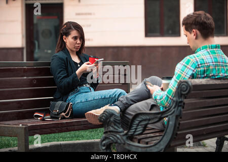 Problema di comunicazione l'uomo con la donna seduta sul banco a via della città di bere il caffè nel bicchiere di carta cercando ito telefoni. concetto di stile di vita. troppo timidi per parlare Foto Stock