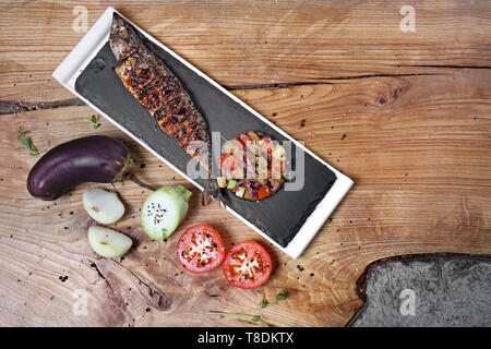 Piastra di ardesia con pesce fritto delizioso e tartare di verdure sul tavolo di legno Foto Stock