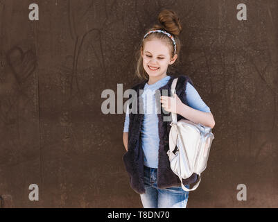 Affascinante otto-anno-vecchia ragazza in un abito alla moda con uno zaino permanente sulla strada in una giornata di sole. Foto Stock