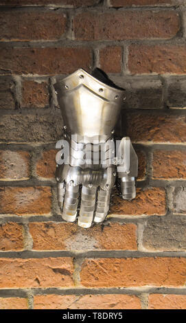 Metallo medievale guanto, un dettaglio di una parte dell'antica armor, dettaglio della guerra. Shining guanto di ferro contro il muro di mattoni in background Foto Stock