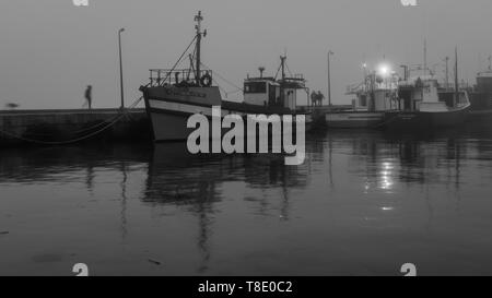 Passeggiate al Crepuscolo per incontrarsi con gli amici come la nebbia rotoli in Hout Bay Harbor nella Penisola del Capo, vicino a Città del Capo in Sud Africa Foto Stock