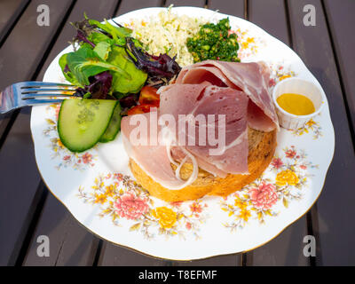 Café pranzo arrosto al miele prosciutto sandwich aperto con senape inglese e contorno di insalata servita all'aperto Foto Stock