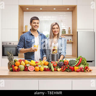 Coppia giovane in posa dietro un bancone cucina riempito con frutta e verdura Foto Stock