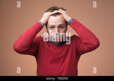 Uomo in maglione rosso nel terrore, tenendo la testa Foto Stock