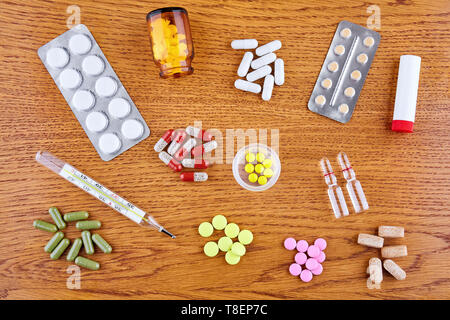 Pillole colorate, capsule, termometro, ampolle e fiale su sfondo di legno. Foto Stock