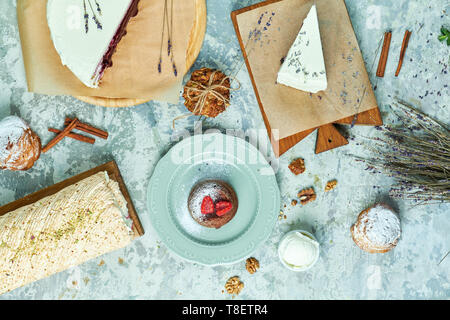 Torte di meringa con lavanda assortimento di diverse torte decorate con frutta su piastre di schede madri e lo sfondo grigio FLATLAY Foto Stock