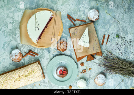 Torte di meringa con lavanda assortimento di diverse torte decorate con frutta su piastre di schede madri e lo sfondo grigio FLATLAY Foto Stock