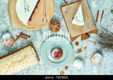 Torte di meringa con lavanda assortimento di diverse torte decorate con frutta su piastre di schede madri e lo sfondo grigio FLATLAY Foto Stock