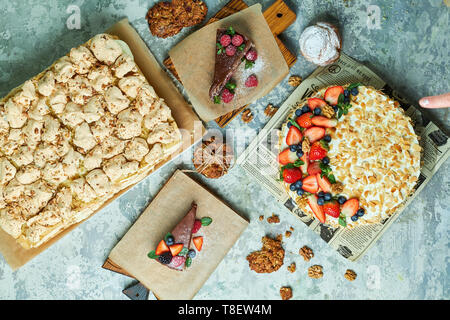 Torte di meringa con lavanda assortimento di diverse torte decorate con frutta su piastre di schede madri e lo sfondo grigio FLATLAY Foto Stock