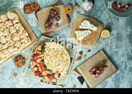 Torte di meringa con lavanda assortimento di diverse torte decorate con frutta su piastre di schede madri e lo sfondo grigio FLATLAY Foto Stock