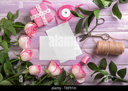 Bellissime rose confezione regalo, materiali di incarto e biglietti di auguri su tavola in legno Foto Stock
