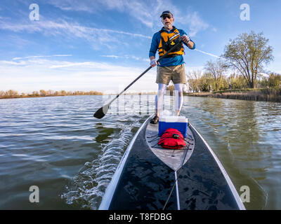 Athletic senior maschio è paddling il suo stand up paddleboard su un lago, POV Immagine con telecamera di azione ampio angolo di distorsione Foto Stock