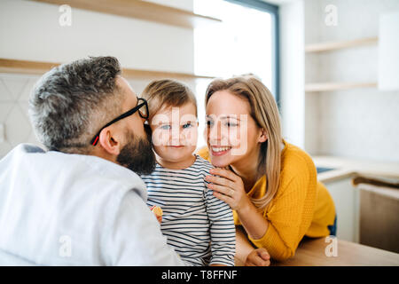 Un Ritratto di giovane famiglia con un bimbo piccolo ragazza in ambienti interni in cucina, baciare. Foto Stock