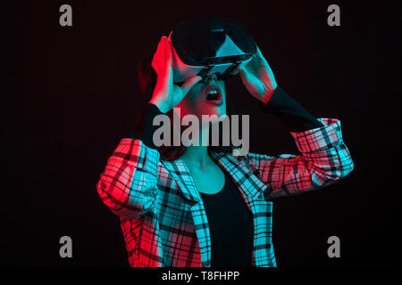 Vista laterale ritratto della bella ragazza adolescente indossando reallity virtuale occhiali con ciano e rosso Colour Gels in studio su sfondo nero. Ragazza adolescente utilizzando moderne techonlogy. Allegro giovane lady utilizzando cuffie vr. Foto Stock