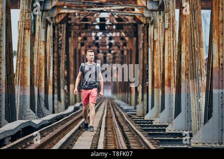 Giovane uomo con zaino camminando sul ponte ferroviario. Temi di avventura, escursioni e viaggi. Foto Stock