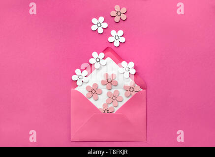 Primavera piatto adagiare sulla carta rosa con effetto decorativo wihte pesche e fiori colorati battenti dalla busta aperta. Millenial sfondo della carta in minimalisti Foto Stock