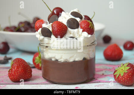 Senza latte e derivati budino di cioccolato in un vasetto con panna montata crema di noce di cocco, guarnita con strawberies e scaglie di cioccolato fondente Foto Stock