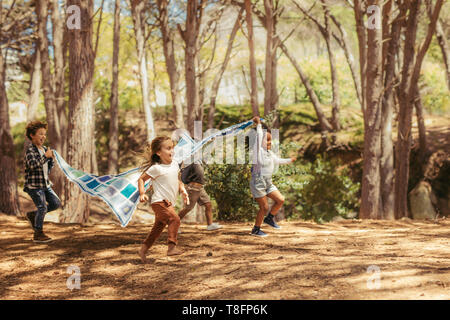 Quattro bambini running nel parco con Coperta picnic. Gruppo di bambini godendo insieme in posizione di parcheggio Foto Stock