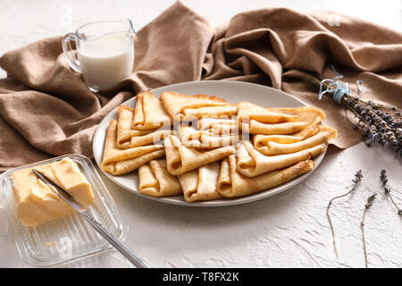 Piastra con gustose frittelle sottili, il burro e la brocca del latte sul tavolo bianco Foto Stock