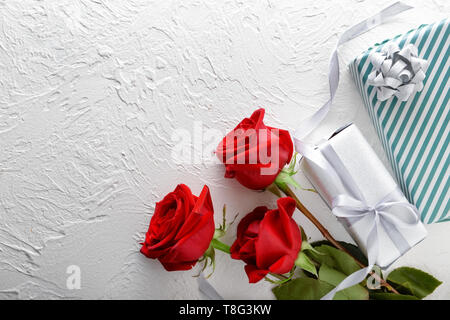 Bellissime rose rosse e confezioni regalo su sfondo chiaro Foto Stock