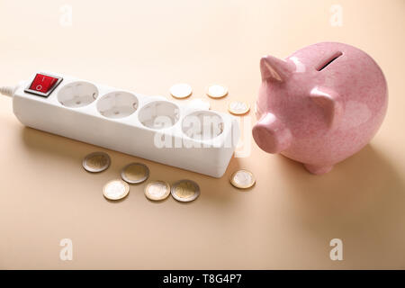 Salvadanaio con monete e il cavo di prolunga sul colore di sfondo. Risparmio di elettricità concept Foto Stock