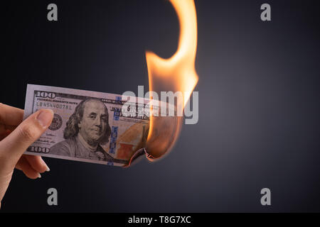 Donna mano che tiene la masterizzazione burning dollar denaro contante su sfondo nero - finanze aziendali, risparmio e concetto di fallimento. Foto Stock