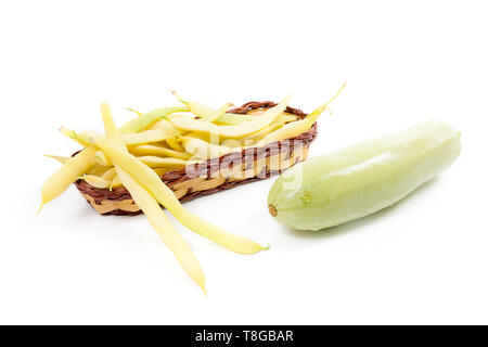 Giallo cesto in legno con giovani baccelli di fagioli con fagioli e zucchine verde con gocce d'acqua isolati su sfondo bianco Foto Stock