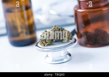 Primo piano di alcune gemme marihuana sul diaframma di uno stetoscopio collocato sul tavolo di un ufficio medici Foto Stock