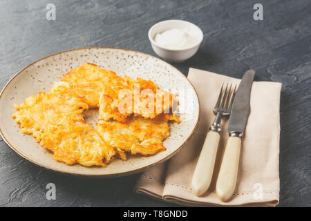 Hommade frittelle di patate - röstinchen, hash browns, kartoffelpuffer, latkes, draniki - con sourcream su sfondo grigio Foto Stock