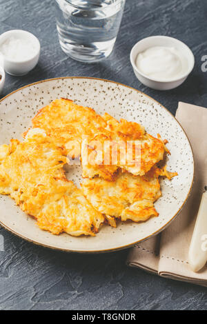 Hommade frittelle di patate - röstinchen, hash browns, kartoffelpuffer, latkes, draniki - con sourcream su sfondo grigio Foto Stock