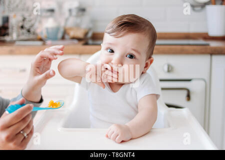 Affascinante piccolo bimbo 6-8 mesi prima di mangiare cibo da zucca cucchiaio a casa Foto Stock