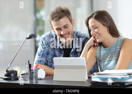 Coppia felice guardando tablet contenuti online seduto su una scrivania a casa Foto Stock