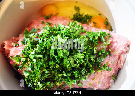 Le polpette di carne non cotti incredients nel recipiente. Carni fresche, uova, prezzemolo, aglio e sale Foto Stock