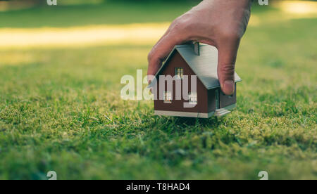 Concetto di vendita di una casa. Una mano è in possesso di un modello di casa sopra il verde prato. Foto Stock