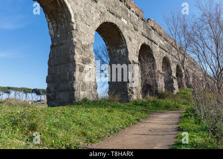 Arcate di un antico acquedotto romano, in blocchi di tufo. Il percorso si snoda lungo la proprietà in un parco verde nella periferia di Roma. Foto Stock