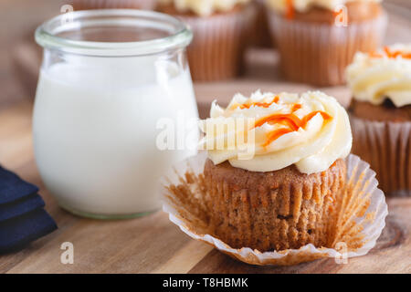 Primo piano della carota cupcake con glassa di formaggio cremoso e un bicchiere di latte e tortine in background Foto Stock