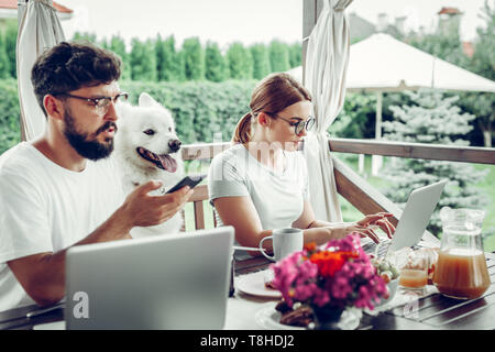Focalizzato donna che lavorano su computer portatile mentre suo marito chiamata di finitura. Foto Stock