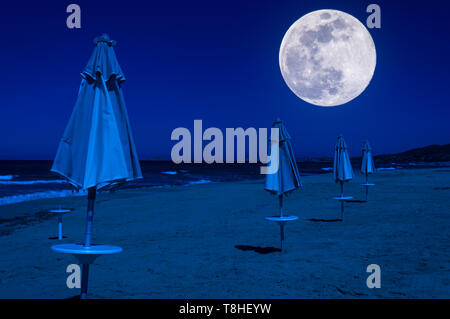 File di ombrelloni e sedie a sdraio sulla spiaggia di notte sotto la luna super Foto Stock