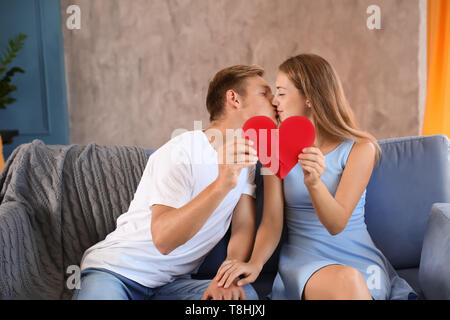 Coppia giovane collega le metà del cuore spezzato sul divano di casa Foto Stock