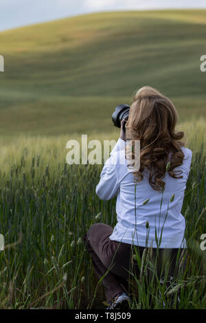 Donna accovacciata in un prato di scattare una foto, San Quirico d'Orcia, Siena, Toscana, Italia Foto Stock