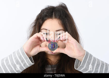 Pretty Girl holding e mostra il cuore nuovo argento cryptocurrency bitcoin in mani su sfondo bianco Foto Stock