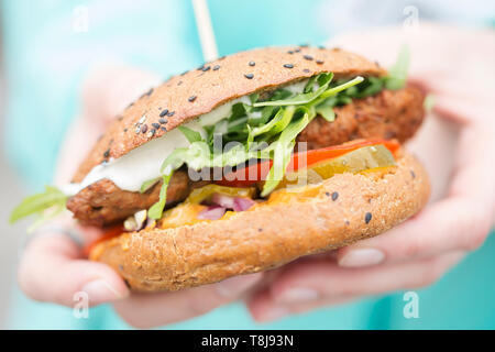 Vegetariano hamburger di manzo con lattuga, pomodoro, cetriolo sottaceto, Formaggio e maionese, mani femminili Foto Stock