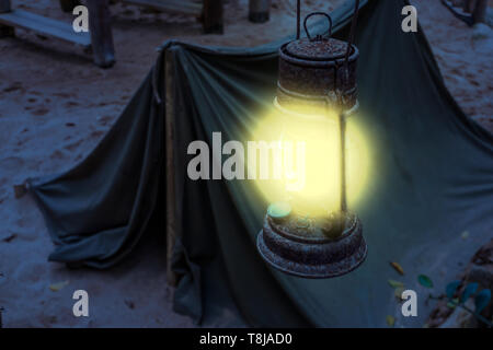 Vecchio arrugginito lanterna illuminata brilla luminosa luce durante la notte, il minatore camp, escursione di Sopravvivenza nella Natura di notte Foto Stock