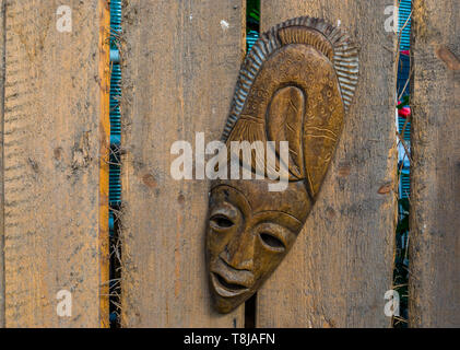 Tradizionale maschera africana appeso su una staccionata in legno, giardino tropicale decorazioni, sfondo nativo Foto Stock